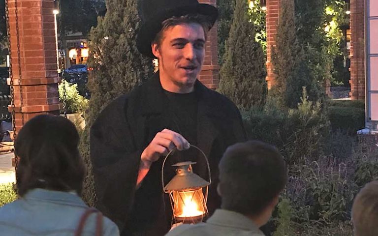 gentleman wearing black top hat and pea coat carries a historic lantern while giving a ghost tour on an original orlando tour
