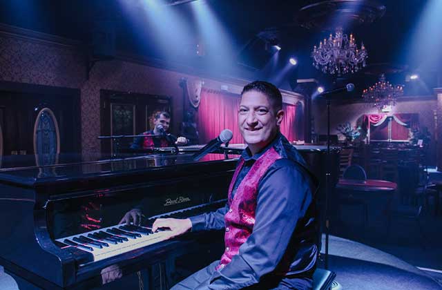 smiling man plays piano across from piano player dueling piano bar beautiful chandelier jewel speakeasy orlando enjoy florida travel blog