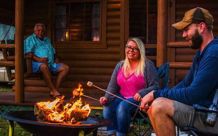 family toasting marshmallows at campfire in front of cabin at st petersburg madeira beach koa holiday
