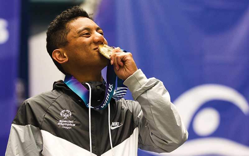 male athlete in a branded jacket kissing a gold medal at the special olympics in oregon