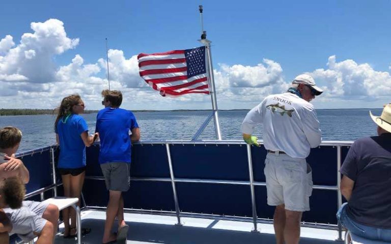 people riding on a boat standing near the rail on deck with a flag at everglades florida adventure