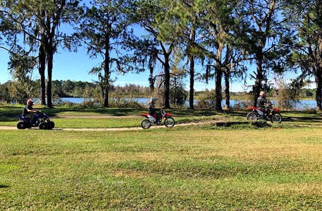 two riders on dirtbikes and an atv rider speeding along a trail at revolution rentals at bone valley atv park