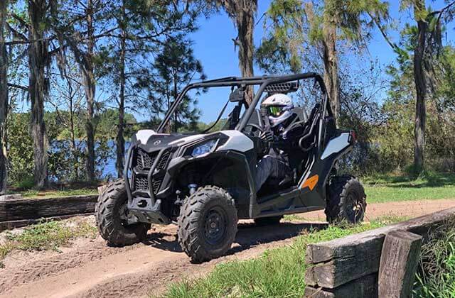 white atv with roll cage and helmeted driver on a forest trail at revolution rentals at bone valley atv park