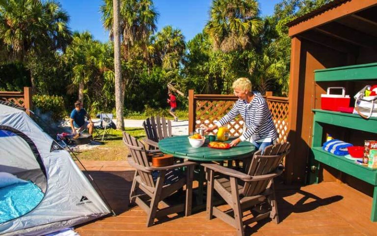 wood patio area with tent table covered area fireplace and man jogging at naples marco island koa holiday