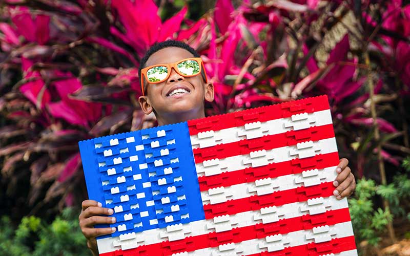 boy smiling with sunglasses holding lego american flag for awe summer at legoland florida