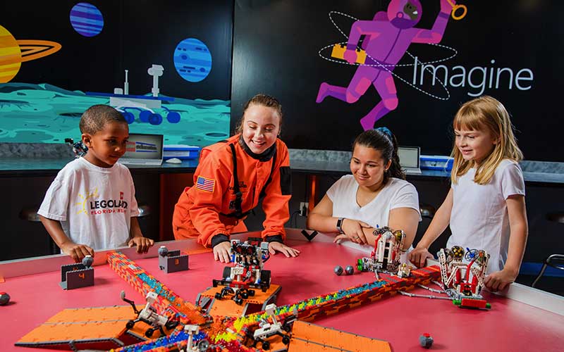 lady in astronaut suit helping kids build lego robot for awesome awe-summer at legoland florida