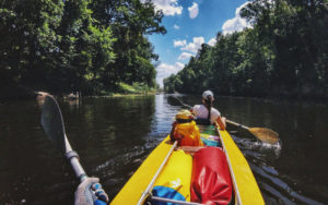 family of three kayaking along green river with trees on banks and cloudy blue sky for incredible kayaking in florida from enjoy florida blog