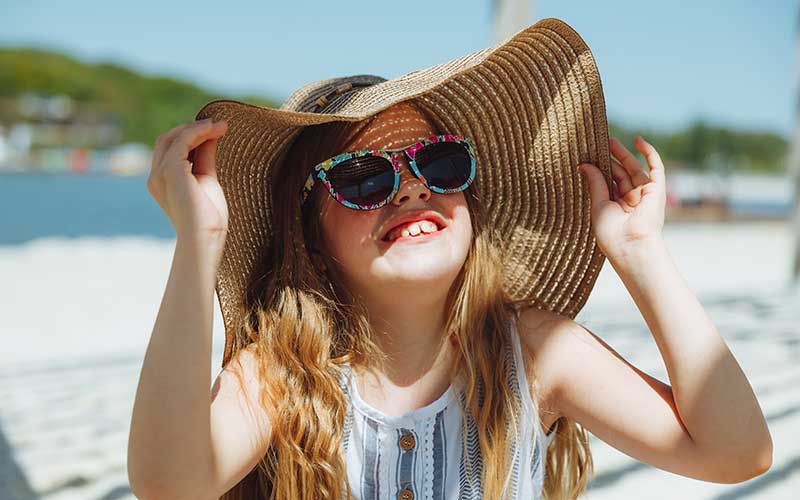 adorable little girl in a hat on the beach for avoiding sunburn for enjoy florida blog