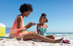 happy mom applying suntan lotion to daughter at beach for avoiding sunburn for enjoy florida blog