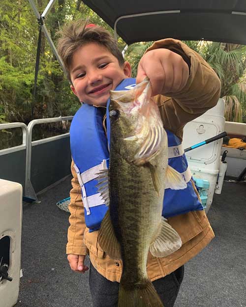 small boy smiling holding up bass for monster bass fishing charters
