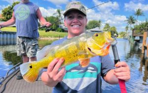 smiling woman holding up large caught bass in boat at dock at florida adventure outfitters miami