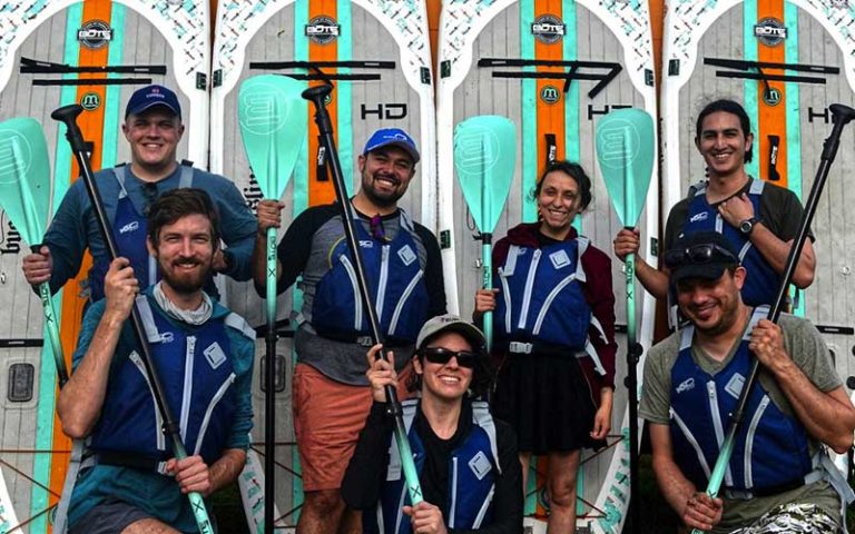 team of paddleboarders group with boards behind them at a paddle in paradise