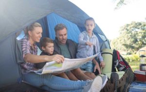 family of four seated inside doorway to tent looking at map with trees for enjoy florida blog