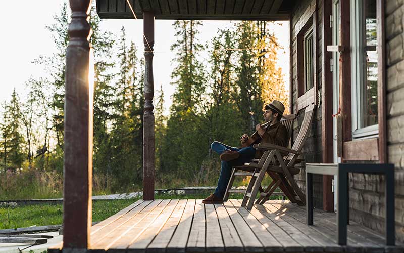 young man with guitar sitting on cabin porch with trees and sunset in background for enjoy florida blog
