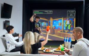 family cheering seated around table eating large screen game at topgolf swing suites