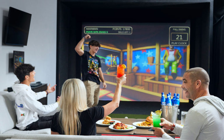 family cheering seated around table eating large screen game at topgolf swing suites