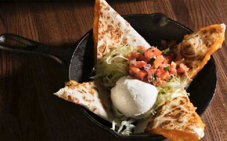 skillet with quesadilla arranged in star pattern with sour cream salsa and lettuce on wood table at brother jimmys icon park orlando