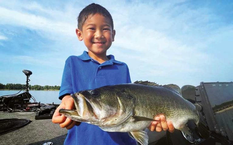 small smiling boy holding huge bass fish on boat at david paycheck fishing