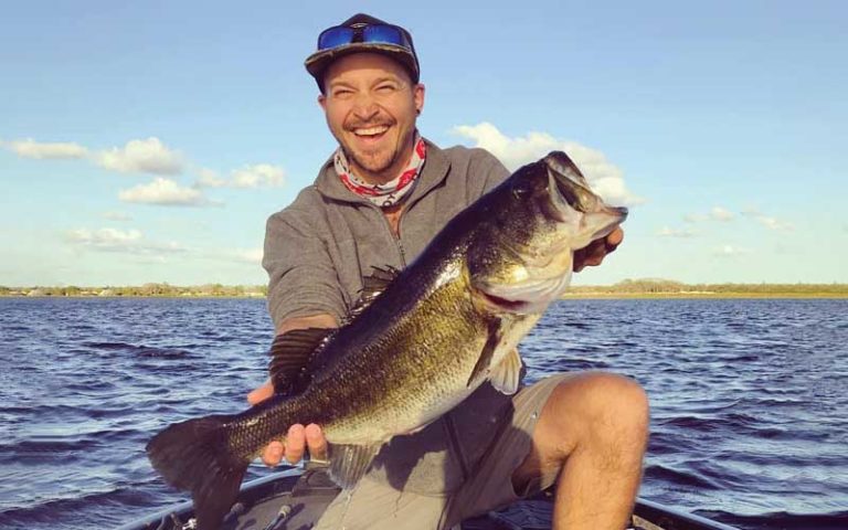smiling man in boat on lake holding up huge bass fish at david paycheck fishing