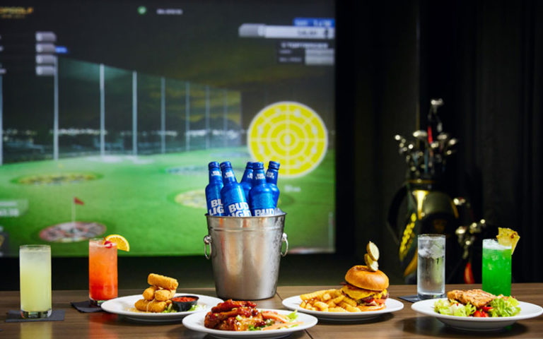 spread of american style food with bucket of beer bottles game on screen at topgolf swing suites