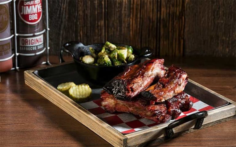 wooden tray with barbecue ribs pickle chips and small skillet broccoli at brother jimmys icon park orlando