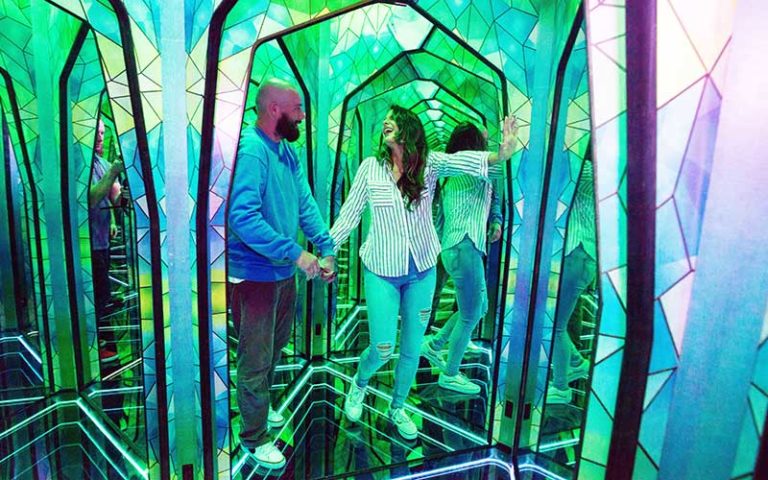 couple walk through mirror maze with green and blue lighting at ripleys mirror maze orlando