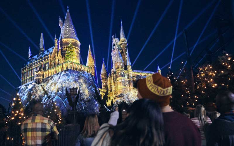crowd at night in warm clothes admiring lit up castle for magic of christmas at hogwarts universal orlando resort
