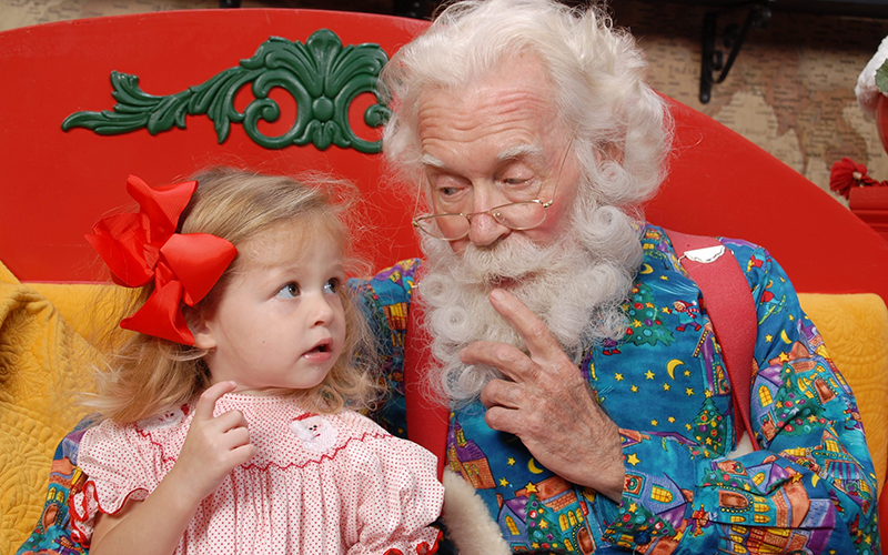 santa character sitting next to small girl at santa workshop experience at icon park