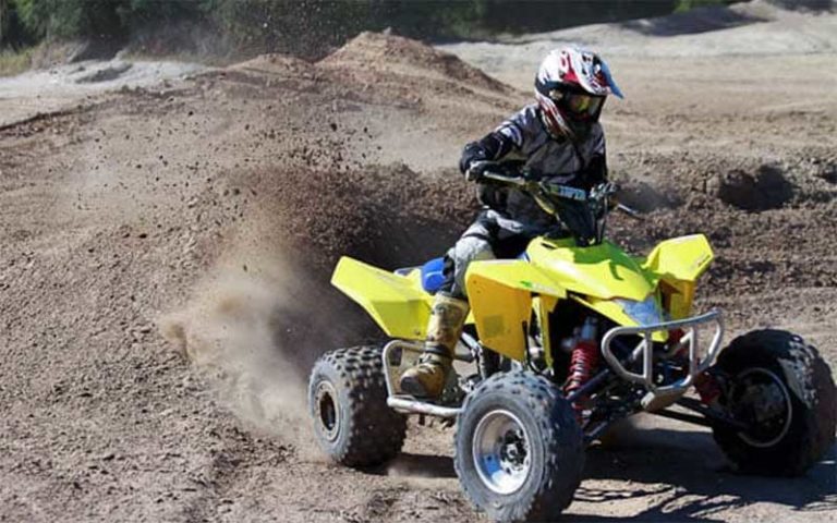 helmeted rider turning yellow atv spraying dirt sand hills at moore atv rentals