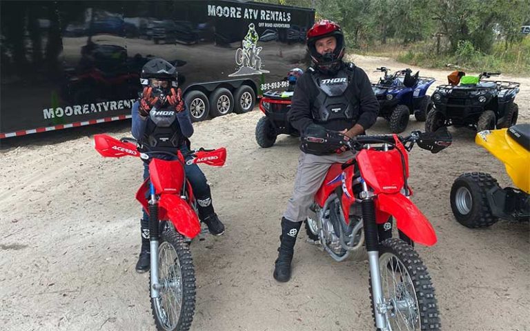 man and boy seated on red dirt bikes with trailer and atvs at moore atv rentals