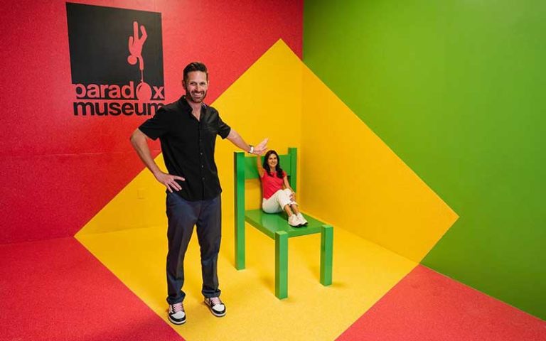 man standing next to chair with tiny woman seated at paradox museum miami