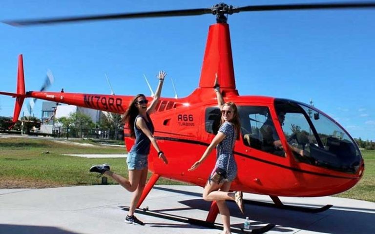 red helicopter on pad with two girls pointing at orlando helicopter adventures kissimmee