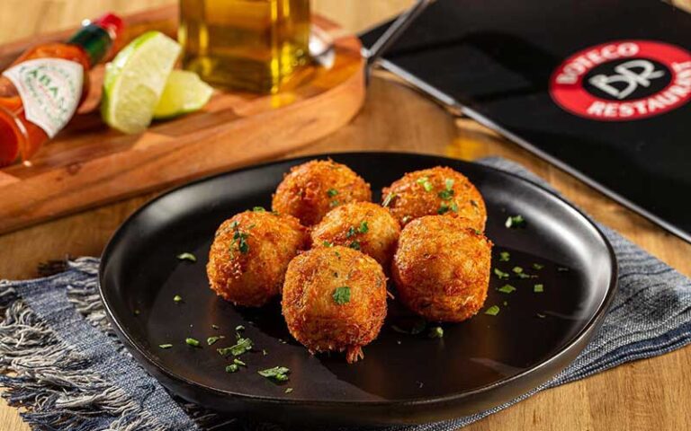 breaded fried balls on black plate with hot sauce bottle limes and logo menu at boteco restaurant orlando