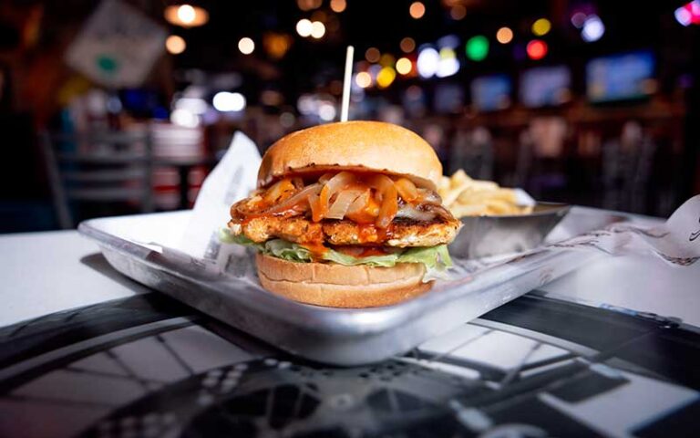 chicken fillet burger with fried onions on metal tray with sports bar background at sickies garage burgers and brews kissimmee