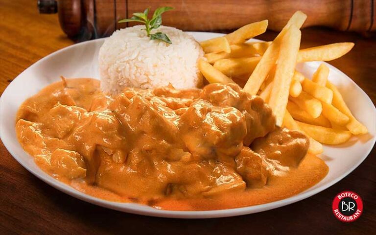 chicken with gravy fries and rice entree on white plate on wood tabletop at boteco restaurant orlando