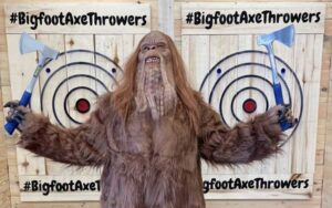 costumed bigfoot holding hatchets in front of wooden targets at bigfoot axe throwing and rage room