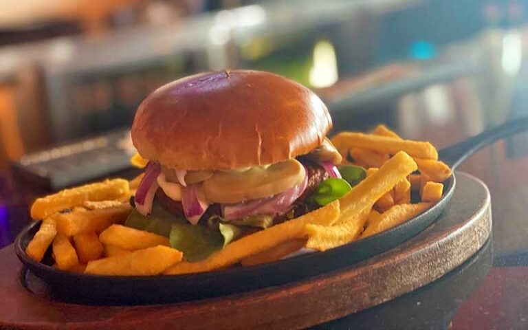 deluxe burger with fries on black frying pan with wood base and bar background at boteco restaurant orlando