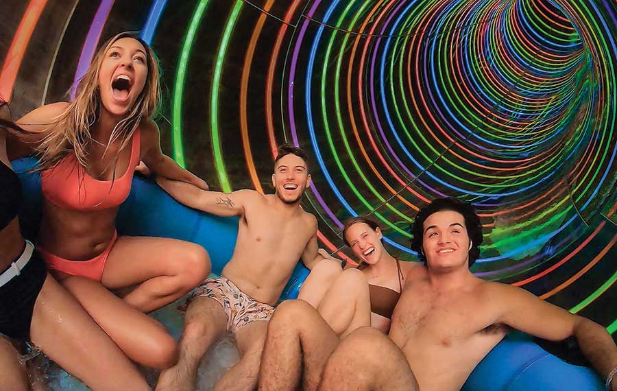 group of teens in swimwear riding a water park tube ride screaming while emerging from black tunnel with multi colored lights at island h2o kissimmee