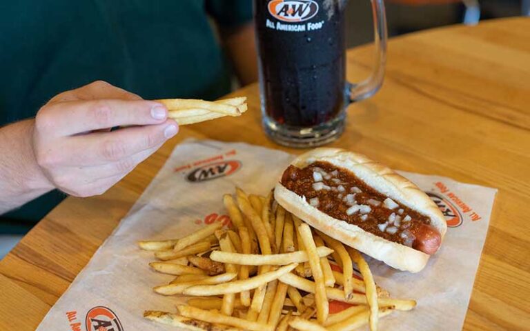 hand holding fries with tabletop meal chili dog fries and mug of root beer at a&w all american food old town