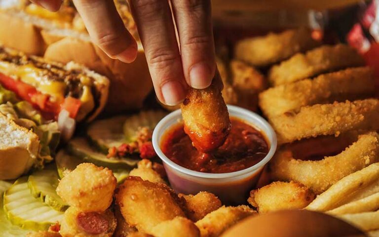 spread of onion rings fries sandwiches burgers with hand dipping into ketchup at a&w all american food old town