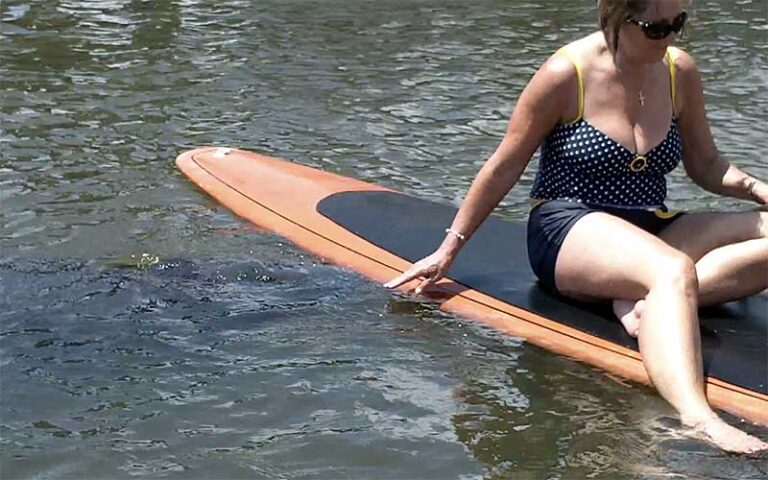 woman in swimsuit sitting on board with hand in water touching manatee at three brothers adventure tours cocoa beach