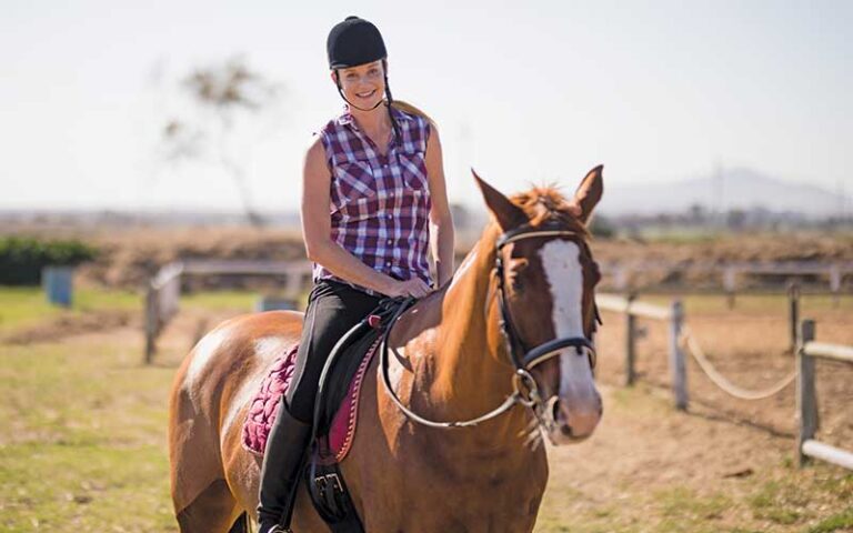 woman with riding helmet smiling on horse with fence at green lakes farm kissimmee