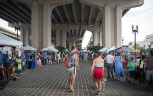 couple walking under bridge with rows of market stalls at riverside arts market jacksonville