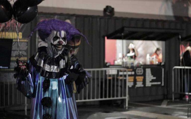 creepy clown with zombie face standing with black balloons at entrance at 13th floor haunted house jacksonville