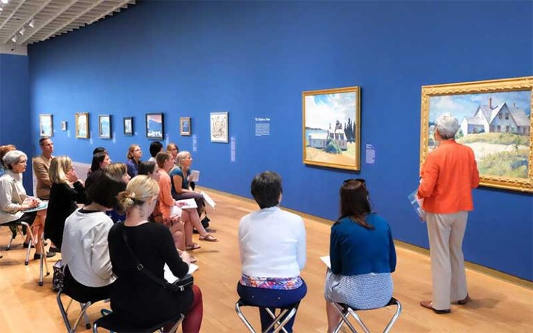 docent speaking to group seated in front of paintings at orlando museum of art