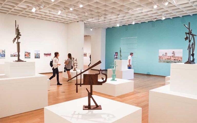 exhibit room with aqua colored wall and white plinths with sculptures at orlando museum of art