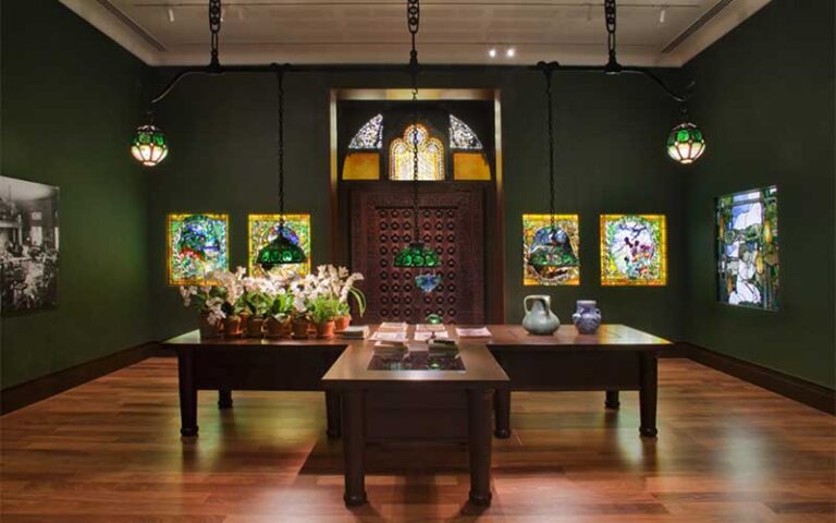 exhibit room with green walls and tables with glassware and art at morse museum orlando