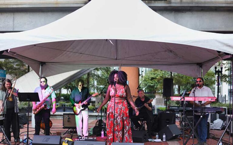female singer at microphone with band under white tent at james weldon johnson park jacksonville
