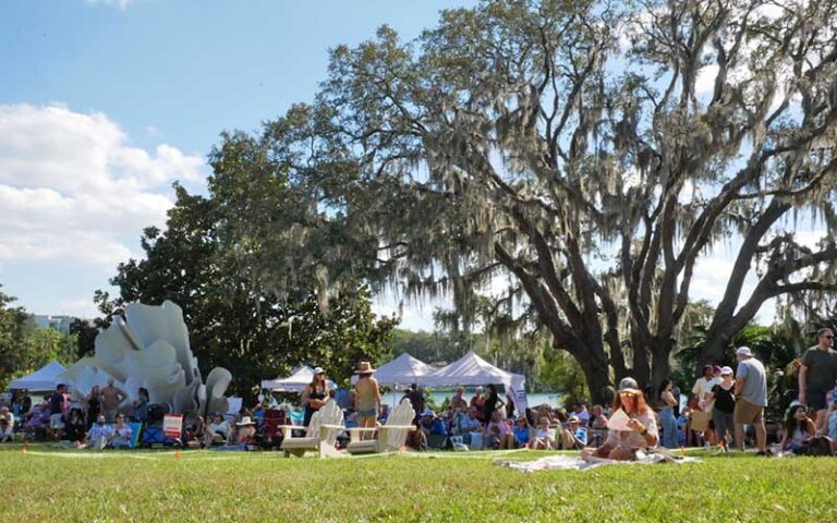 grassy area with oak trees crowds tents and white sculpture at mennello museum orlando