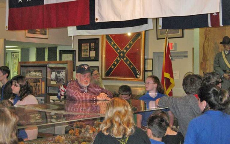 man standing behind glass cases of antiques with kids walking around at museum of southern history jacksonville